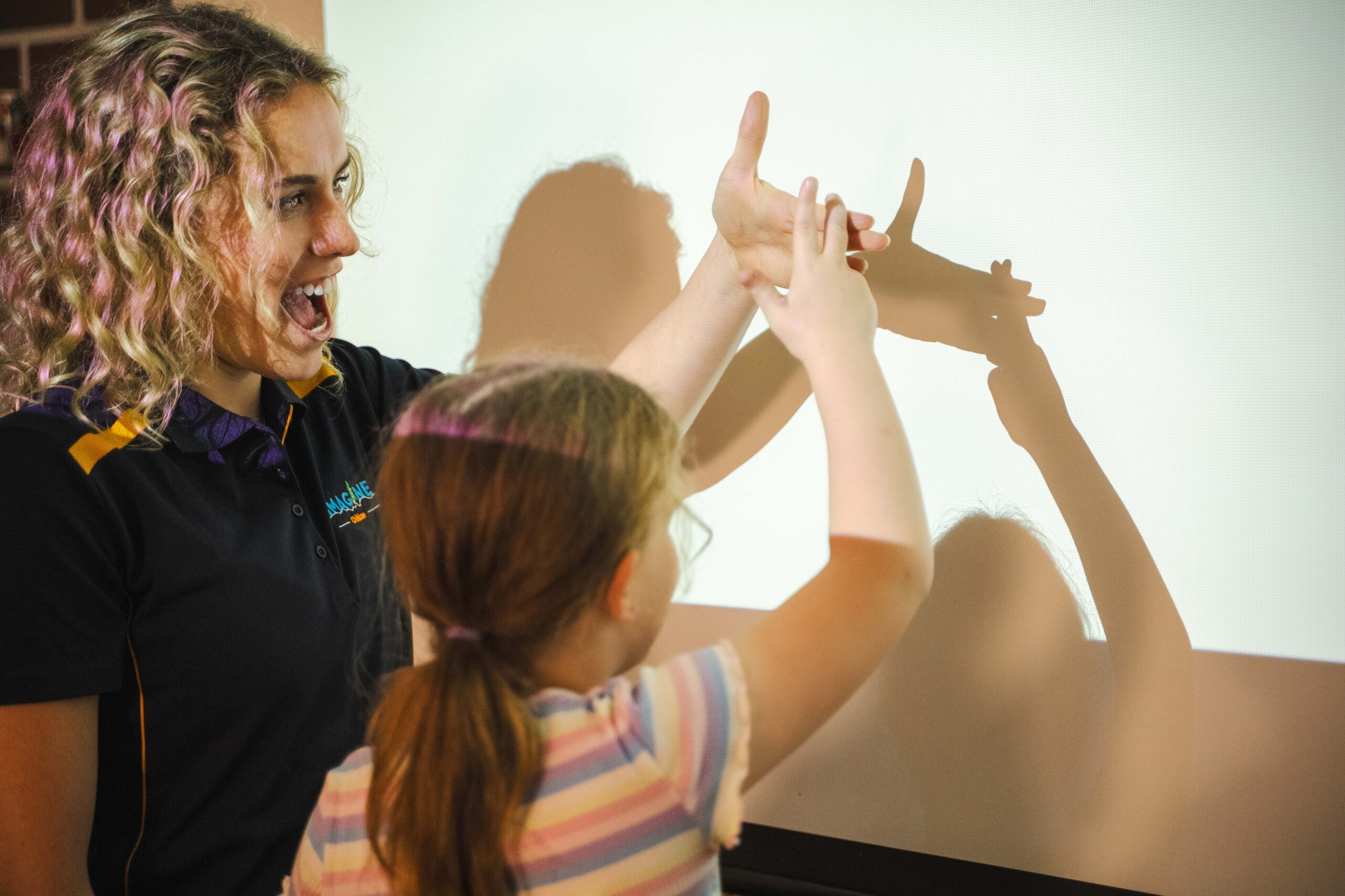 An Imagine Childcare educator and child make hand shadows during a STEAM learning experience